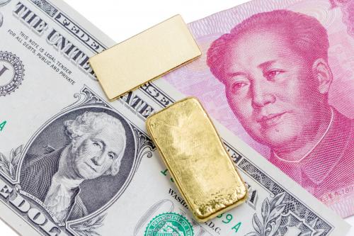 Gold bar over the US dollar bill and Chinese yuan banknote on white background, economy finance concept.